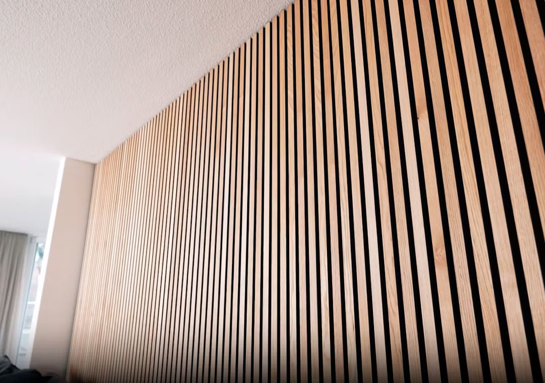 Nahaufnahme einer Akupanel-Akustikholzplatte mit vertikalen Holzlamellen in einem gestreiften Muster, die an einer Innenwand unter einer weißen Decke angebracht ist.